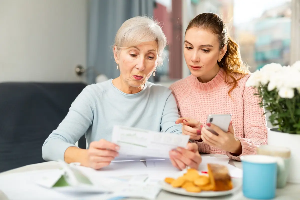 signs your elderly parent needs assisted living - Adult daughter helping elderly mother review documents at home